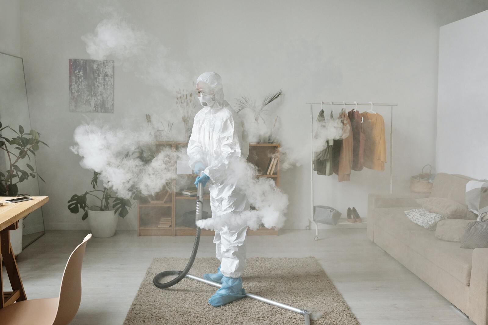 Frau in Chemikalienschutzkleidung, die in einer Wohnung Chemikalien versprüht