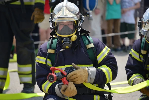 Feuerwehrmänner in voller Montur, vordere Person hält Feuerwehrspritze