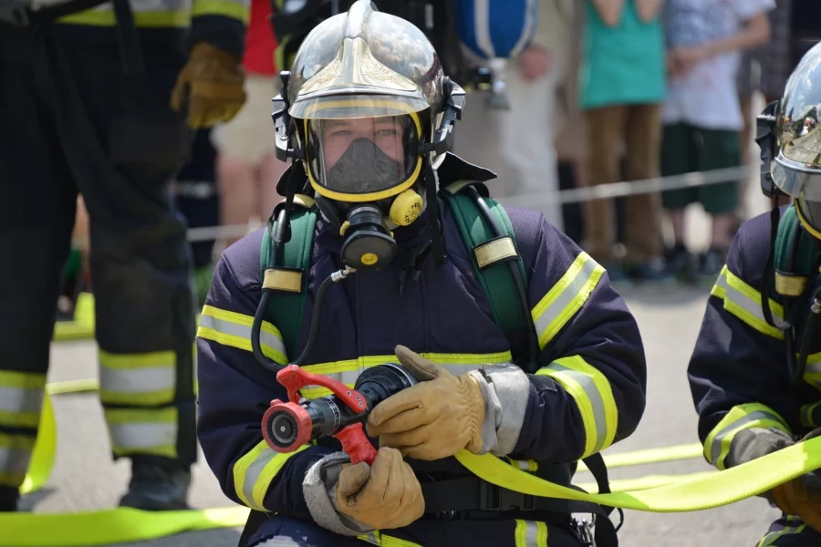 Feuerwehrmänner in voller Montur, vordere Person hält Feuerwehrspritze