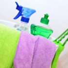 Reinigungsutensilien, darunter ein grünes und ein lila Mikrofasertuch, eine Sprühflasche und eine grüne Seifenflasche