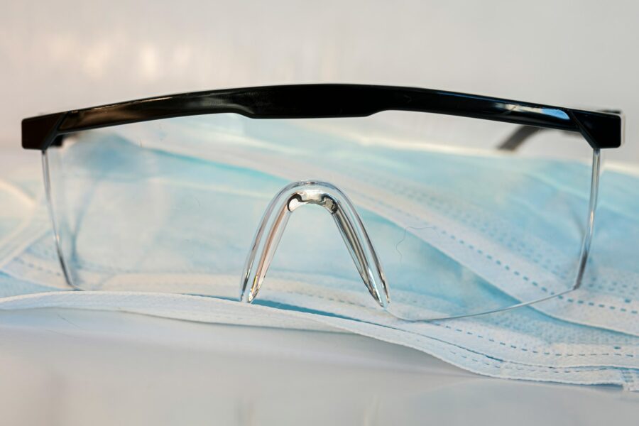 Schutzbrille liegt auf einer chirurgischen Maske auf einem weißen Untergrund.